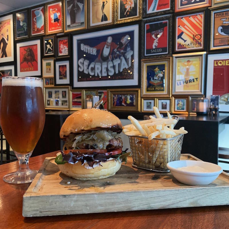 a board with the Bistro burger, fries and truffle mayonnaise with a pint of beer on a table inside Bistro Felix